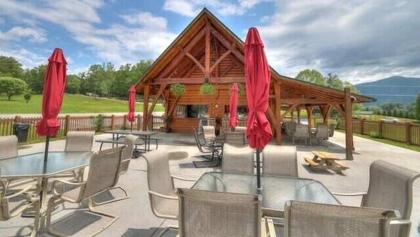Eine Holzlodge mit überdachter Terrasse, die Sitzgelegenheiten und Sonnenschirme bietet.