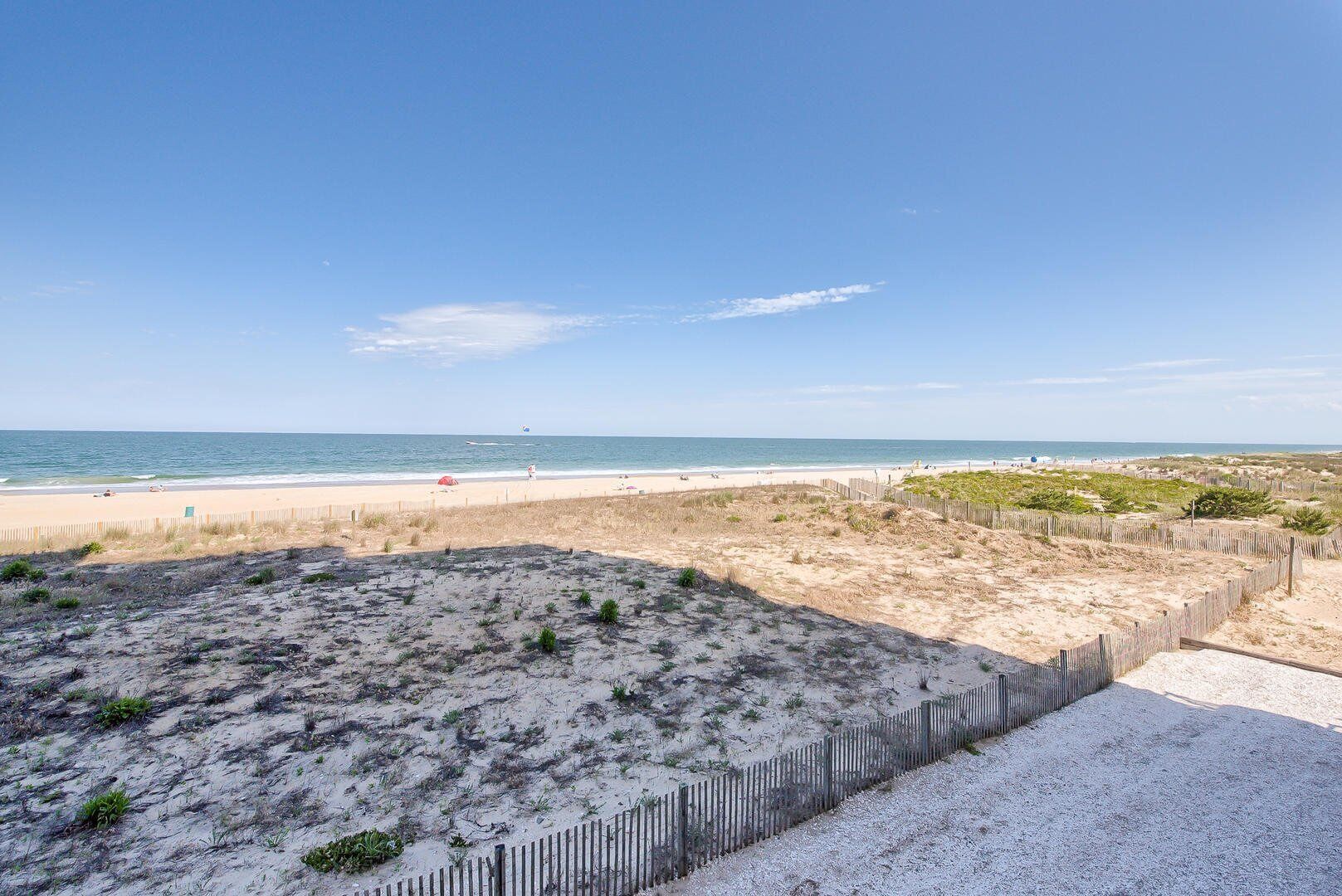 A beach with a sandy path leading to the water, a wooden fence, and sparse vegetation.
