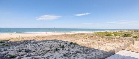 A beach with a sandy path leading to the water, a wooden fence, and sparse vegetation.