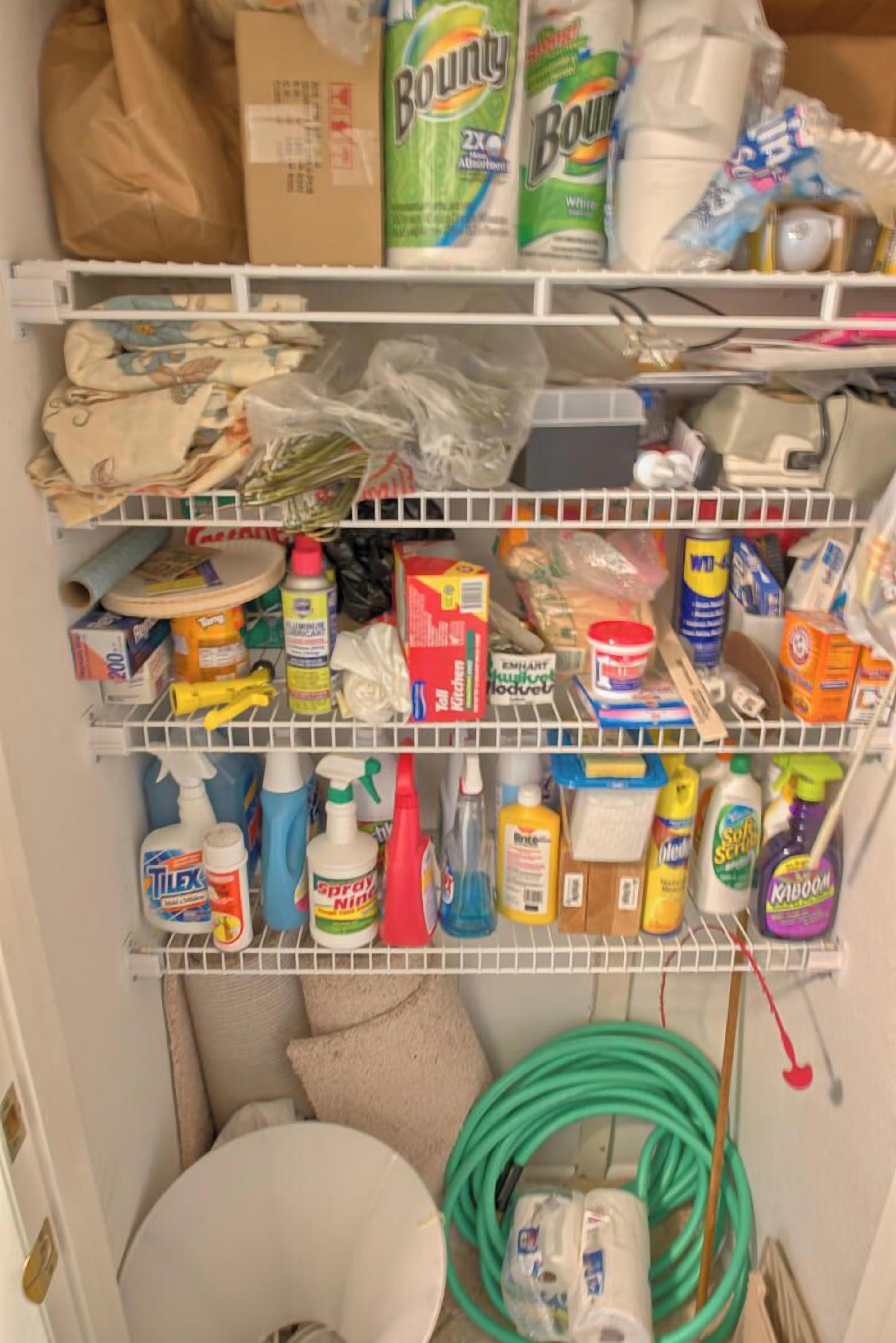 A storage area with shelves containing cleaning supplies, a toilet paper roll, and a coiled garden hose.