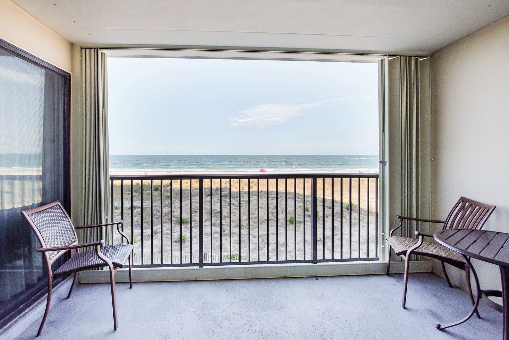 A balcony with a view of the beach and ocean. There are two chairs and a table.