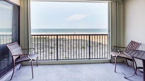 Un balcon avec vue sur la plage et l’océan. Il y a deux chaises et une table.
