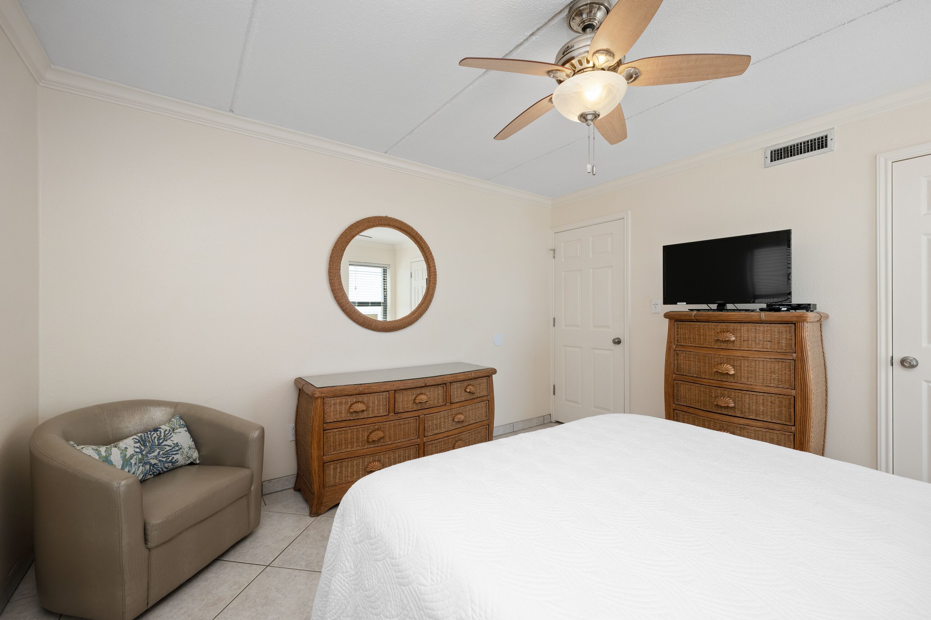 A bedroom with a bed, a dresser, a television, a ceiling fan, and a chair.