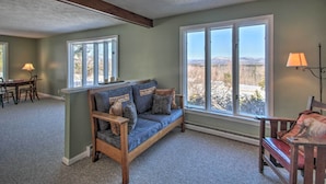 A cozy living room with a sofa, a dining table, and large windows offering a view of the outdoors. - Parsonsfield Vacation Rental Near Skiing & Lakes! (Parsonsfield)