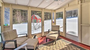 A sunroom with a ceiling fan, large windows, a red barn visible outside, and a red floor. - Parsonsfield Vacation Rental Near Skiing & Lakes! (Parsonsfield)