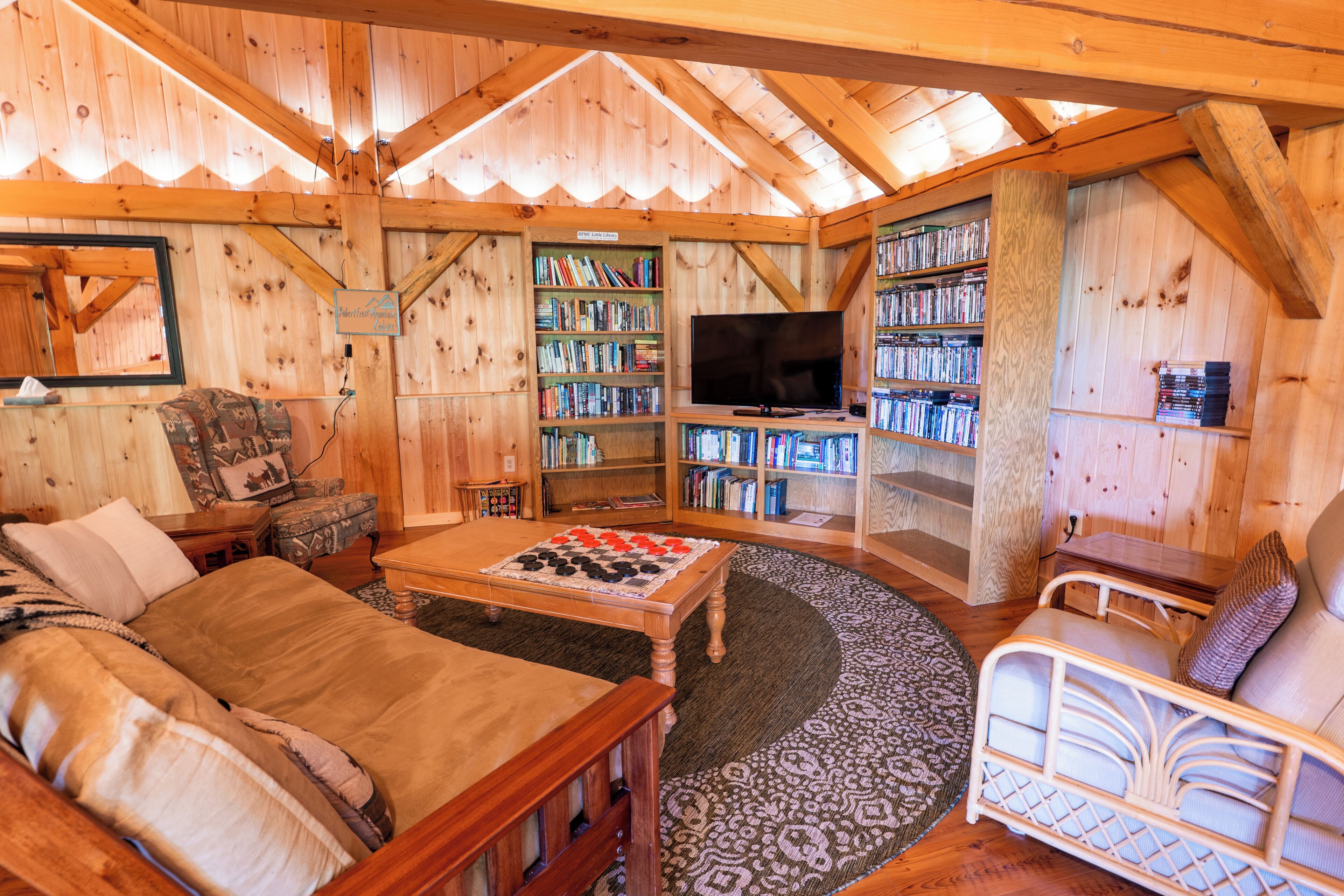 A cozy cabin interior with a living room, a bookshelf, a television, and a crib.