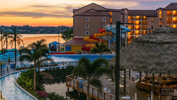 A resort pool area with a water slide, palm trees, and a thatched-roof structure. - Platinum Presidential Lock-Off Villa on the Lake-Westgate Lakes Orl. Sleeps 16 (Orlando)