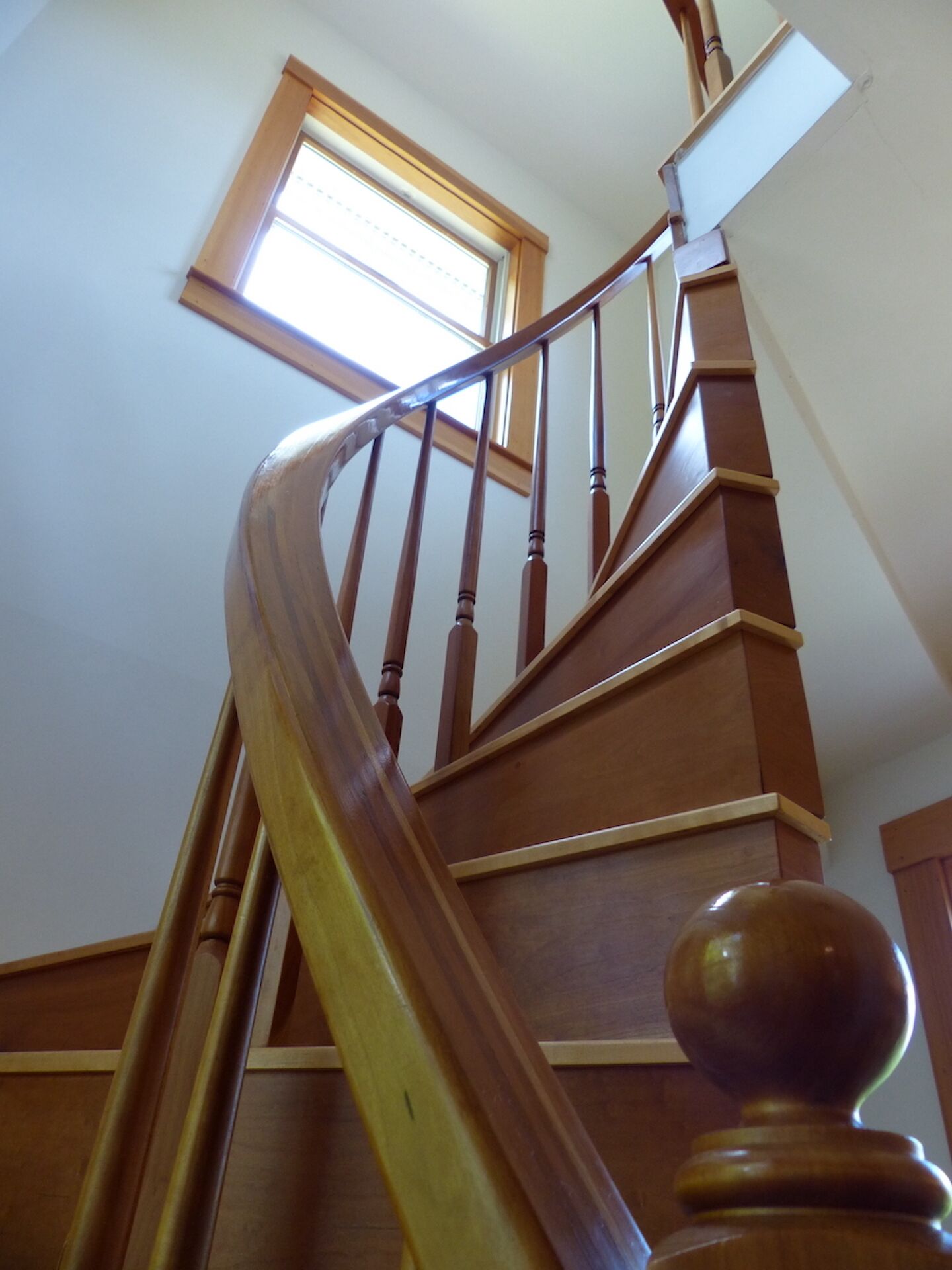 A wooden staircase with a curved handrail and a window at the top.