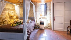 A bedroom with a stone wall, a bed with a canopy, a nightstand with a lamp, and a door.