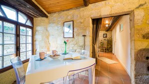 A rustic stone interior with a wooden ceiling, a table with a glass top, and a chair.