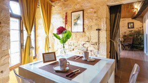A rustic stone wall interior with a dining table set for two, a vase with a flower, and a framed picture on the wall.