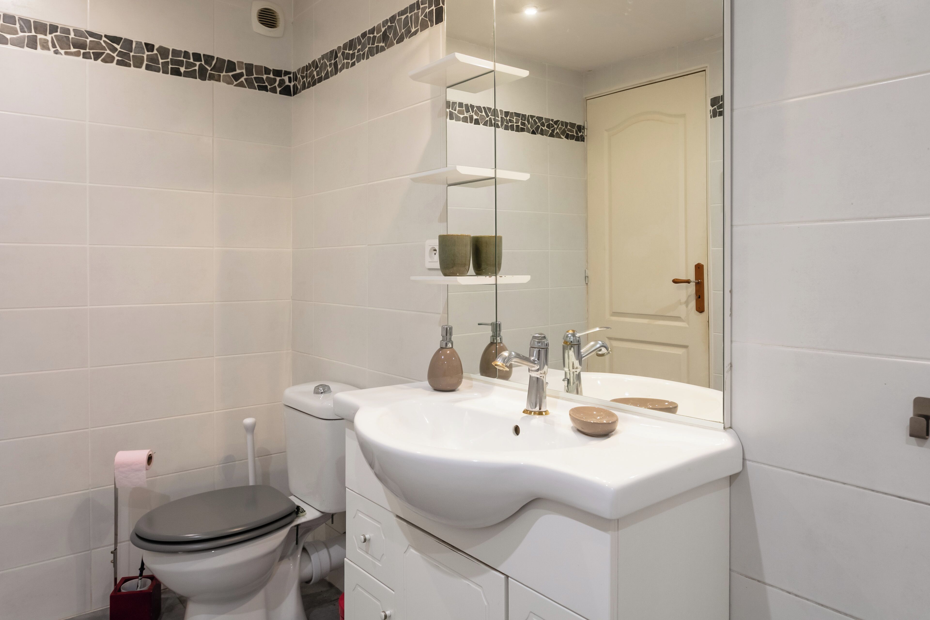 Une salle de bain équipée de toilettes, d’un lavabo, d’un miroir et d’une étagère contenant des articles de toilette.