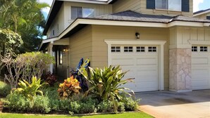 A two-story house with a garage, surrounded by well-maintained landscaping including various shrubs and a lawn. - Hawaiian Escape with all the Amenities  (Kapolei)