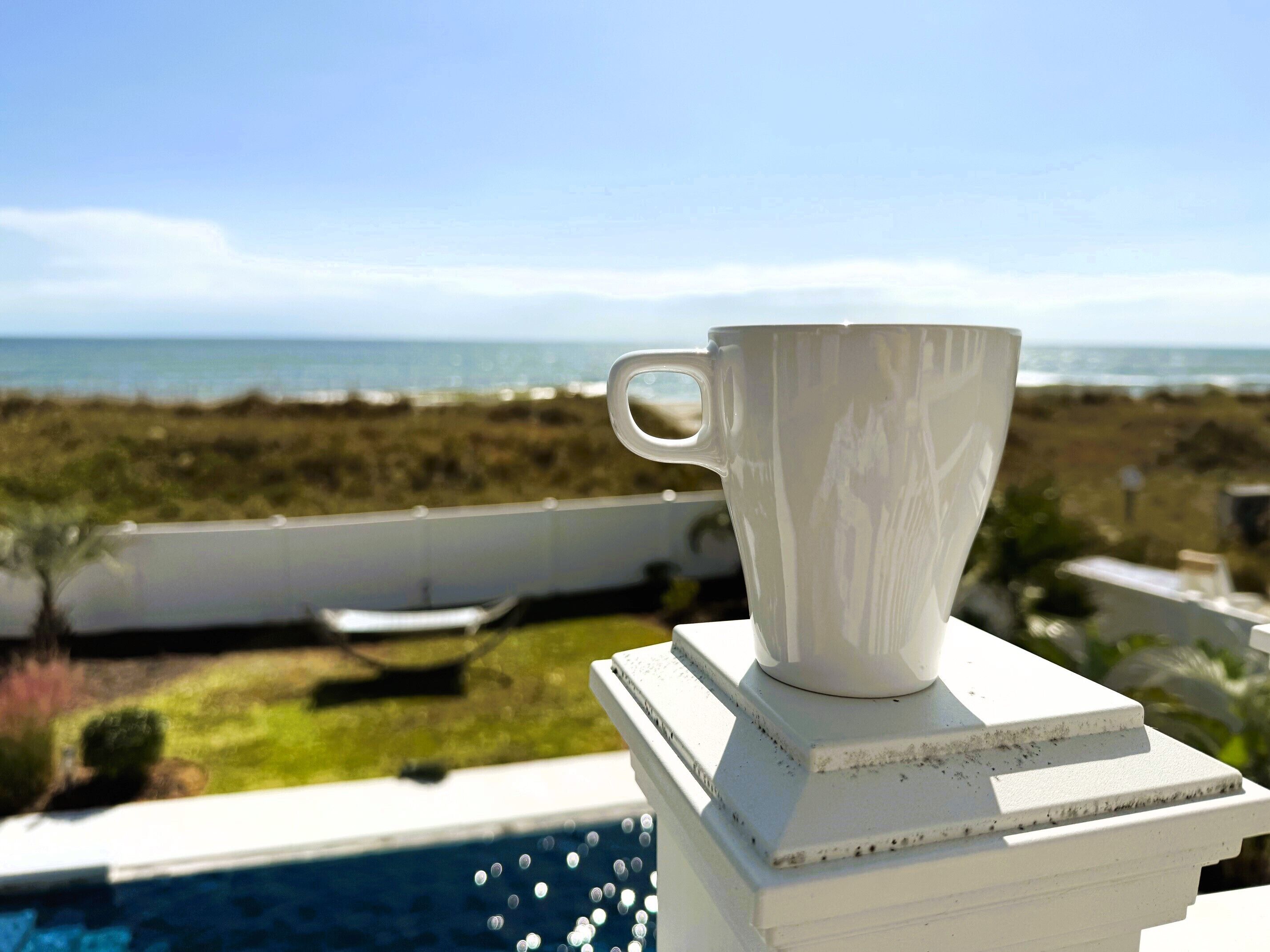 A white cup on a white pedestal with a view of a pool and ocean in the background.