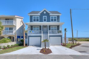 Une propriété de deux étages située en bord de mer, dotée d’un porche à l’avant, d’un garage et d’un petit espace paysager agrémenté de palmiers.