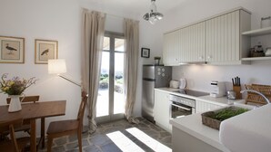 Una cocina compacta con suelo de piedra, una zona de comedor con mesa y sillas de madera, y vistas a través de un ventanal.