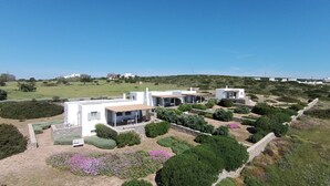 Une maison moderne dotée d’un patio, entourée de jardins aménagés et d’un paysage vallonné.