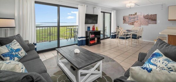 A modern living room with a large sliding glass door to a balcony, a dining area, and a TV mounted on the wall.