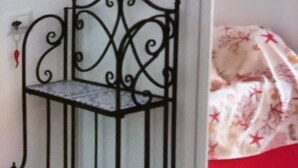 Une étagère métallique à trois niveaux, adossée à un mur, à côté d’un lit doté d’une tête de lit rouge.