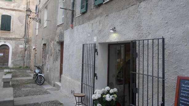 Une rue étroite, avec un immeuble orné d’une grille en métal, un scooter garé devant et une petite table décorée de fleurs.