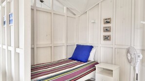 Habitación con una cama individual, colcha a rayas, almohada azul y mesita de noche blanca. Hay tres cuadros enmarcados en la pared.