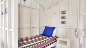 A single-bed room with a striped bedspread, a blue pillow, and a white nightstand. There are three framed pictures on the wall. - Jack s Cottage - perfect Wooli escape (Wooli)