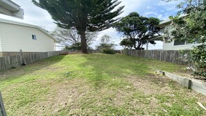 A fenced backyard with a large tree, a wooden fence, and a grassy area.