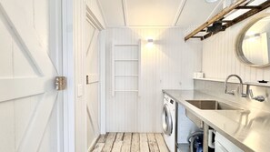 A compact laundry room with a washing machine, a sink, and a wooden ladder.