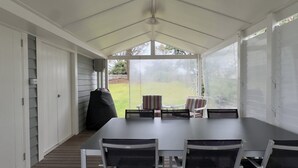 Un patio techado con una mesa, sillas, una parrilla y vistas al jardín.