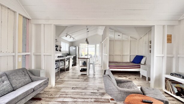 Una habitación amplia con piso de madera, un sofá, una silla, una cama y una zona de cocina.