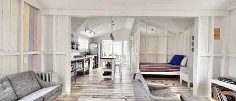 A spacious room with a wooden floor, a sofa, a chair, a bed, and a kitchen area.
