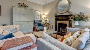 A living room with a fireplace, a large mirror, and a blue armchair. - Rawlinson Road 10B | Oxford Holiday Let | 2 Beds & Sleeps 4 (Oxford)