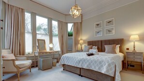 A bedroom with a large bed, a vanity with a mirror, a chair, and a desk. - Rawlinson Road 10B | Oxford Holiday Let | 2 Beds & Sleeps 4 (Oxford)