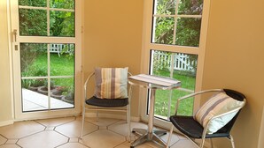 A corner room with two chairs, a small table, and large windows offering a view of a garden.