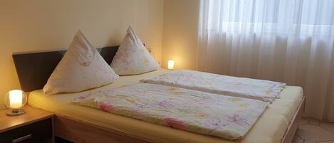 A double bed with floral bedding, two pillows, bedside lamps, and a nightstand with a drawer.