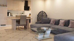 A modern living room with a grey sofa, a glass coffee table, and a kitchen area with a white countertop and wooden cabinets.