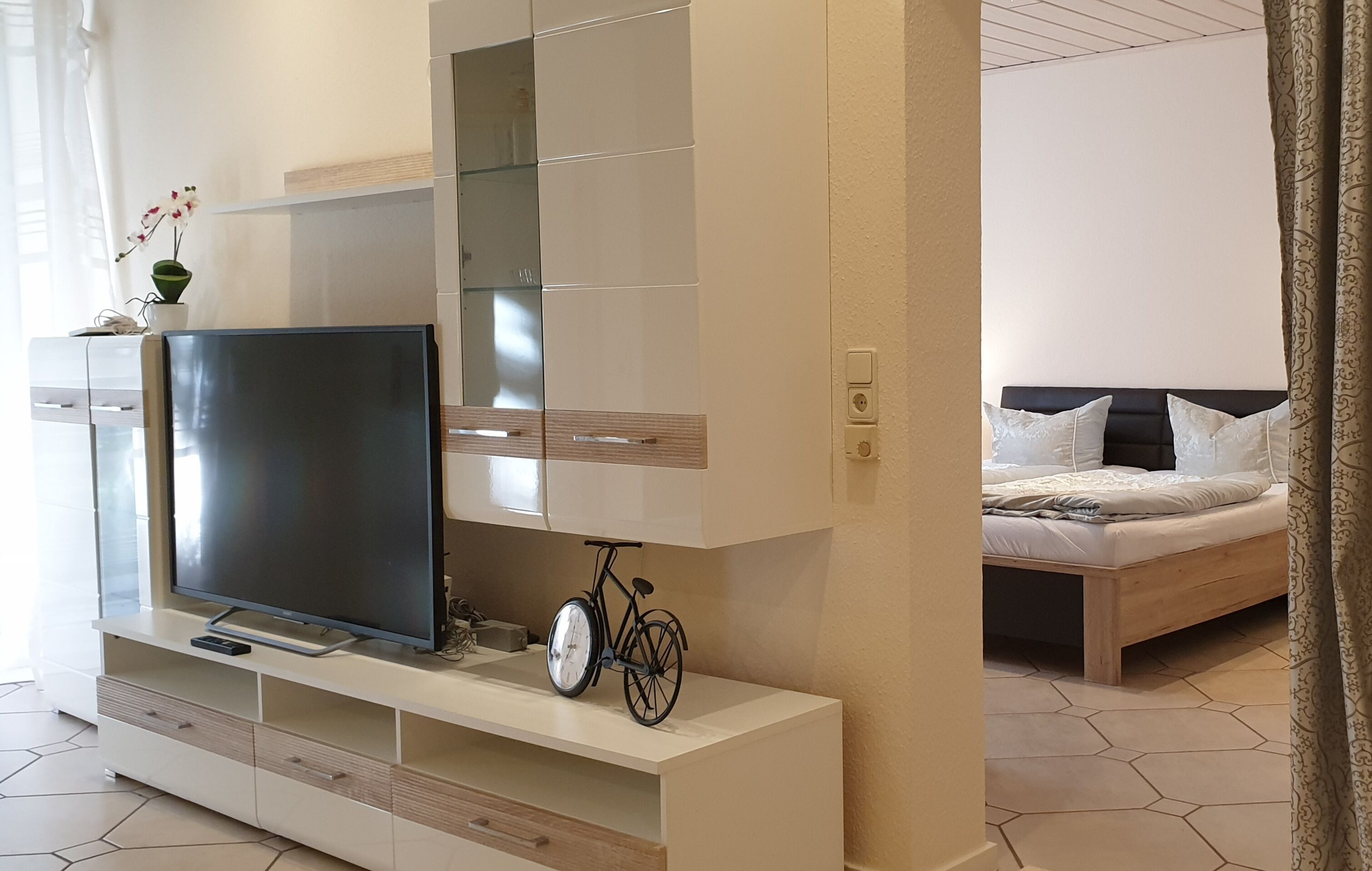 Une chambre moderne avec une télévision posée sur une console blanche, un vélo et un lit doté d’une tête de lit.
