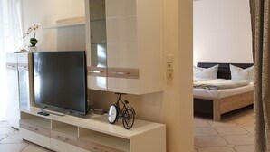 A modern bedroom with a TV on a white console, a bicycle, and a bed with a headboard.