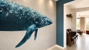 A room with a large whale mural on the wall, a seating area with leather chairs, and a large window with curtains. - Minnie Beach House, TOP NOTCH (Minnie Water)