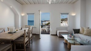 A spacious living area with a dining table, a sofa, and a balcony with a view of the sea and buildings.