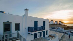 A white building with a balcony, a staircase, and a view of windmills in the background.