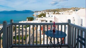 A balcony with a table and chairs overlooking a coastal town with white buildings and a view of the sea.