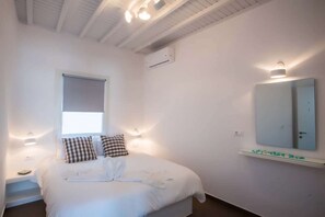 A bedroom with a bed, a window, a wall-mounted mirror, and a ceiling light fixture.