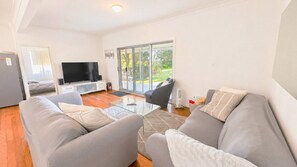 A modern living room with a flat-screen TV, grey sofas, and a glass coffee table. - On The Beach - located on the sand dunes. (Wooli)