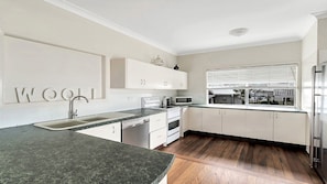 A modern kitchen with white cabinets, a granite countertop, a stainless steel refrigerator, and a window with blinds. - On The Beach - located on the sand dunes. (Wooli)