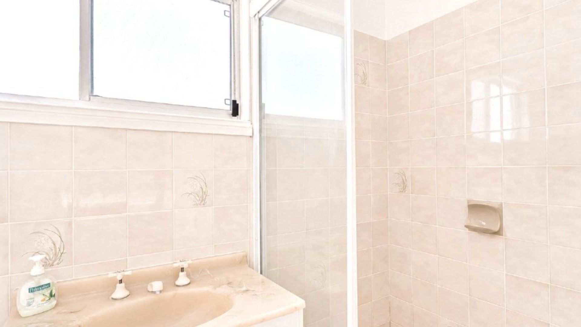 A bathroom with a sink, two faucets, a soap dispenser, and a mirror.