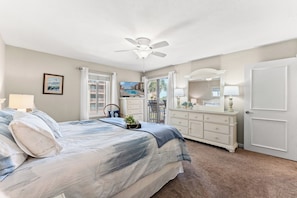 A bedroom with a bed, dresser, ceiling fan, and a window with curtains.