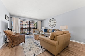 A living room with a sofa, armchair, coffee table, and a large window with a view of buildings.