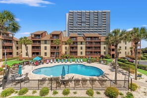 A hotel with a swimming pool, outdoor seating, and a tall building in the background. - Anchorage II 205  Lovely 2 Bedroom Condo With Great Ocean Views and Outdoor Swimming Pool (MYRTLE BEACH)