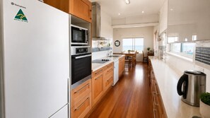 A modern kitchen with wooden cabinets, a stainless steel refrigerator, and a view of the sea through the window.